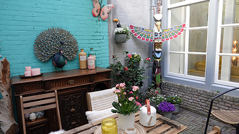 Het terras van de studio met turquoise muur, houten meubels en veel planten