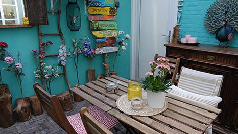 Zithoek op het terras met een tafel van pallethout, stoelen en een turquoise muur