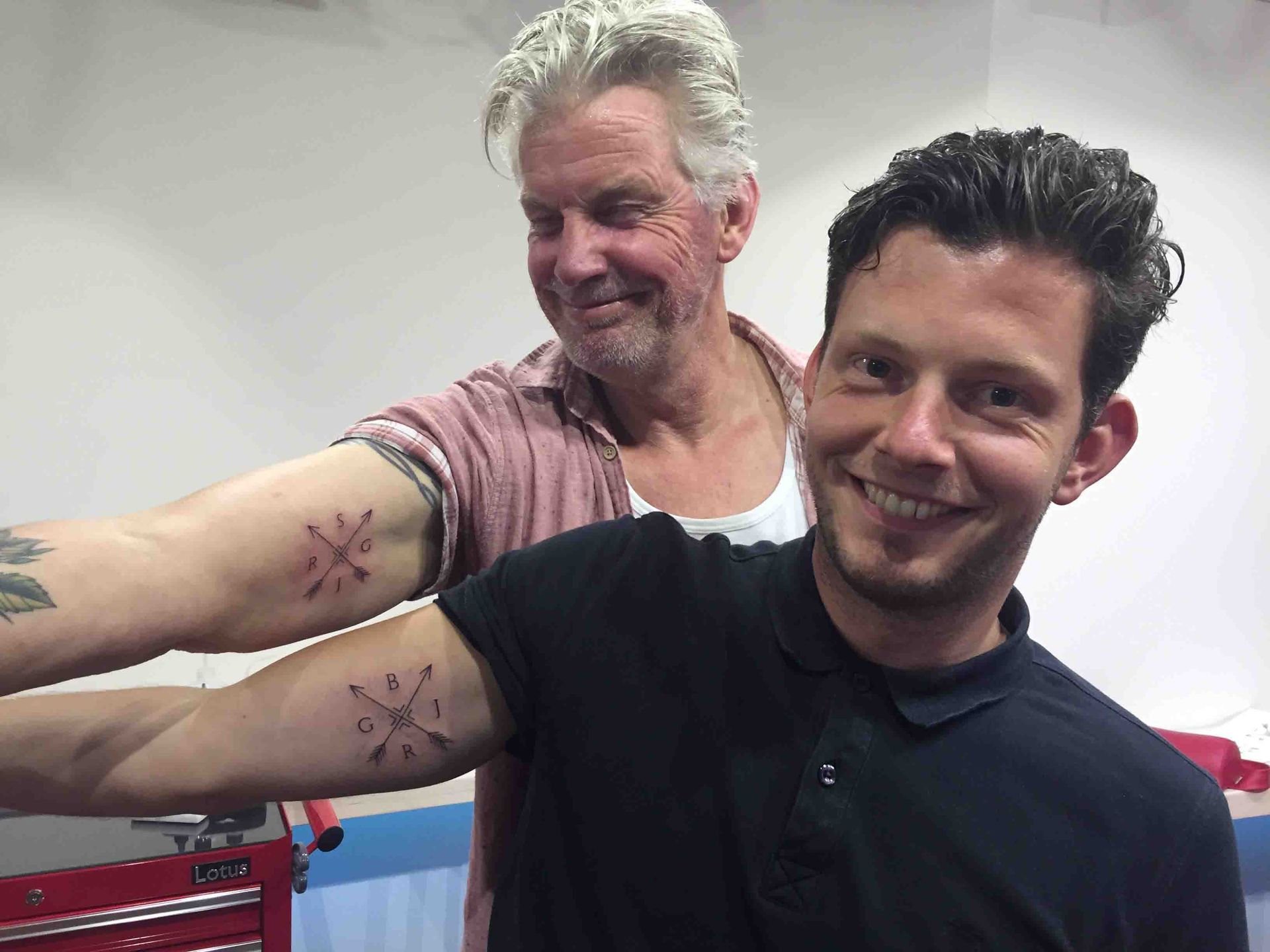 Twee mannen laten lachend hun gelijke tatoeage op de onderarm zien