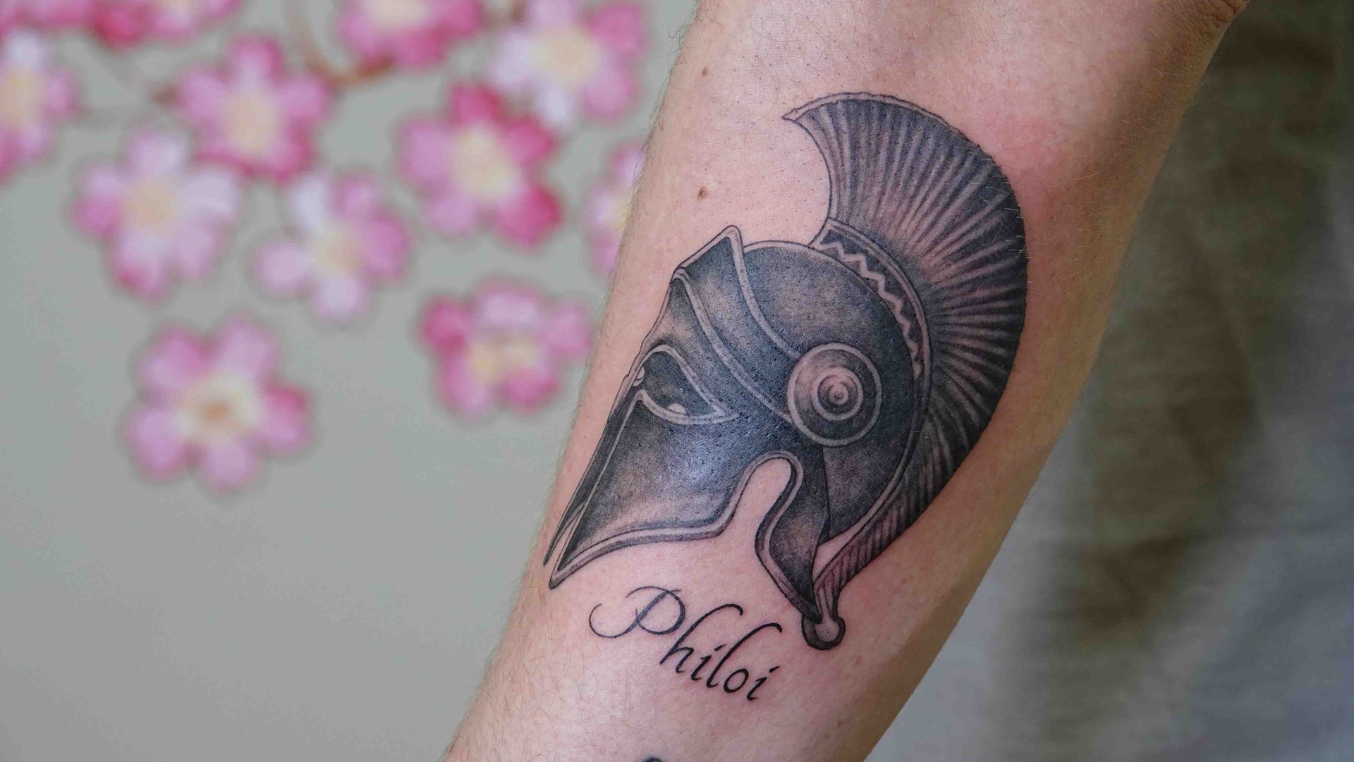 Spartaanse helm in zwart-grijs op een onderarm, met de naam Philot eronder