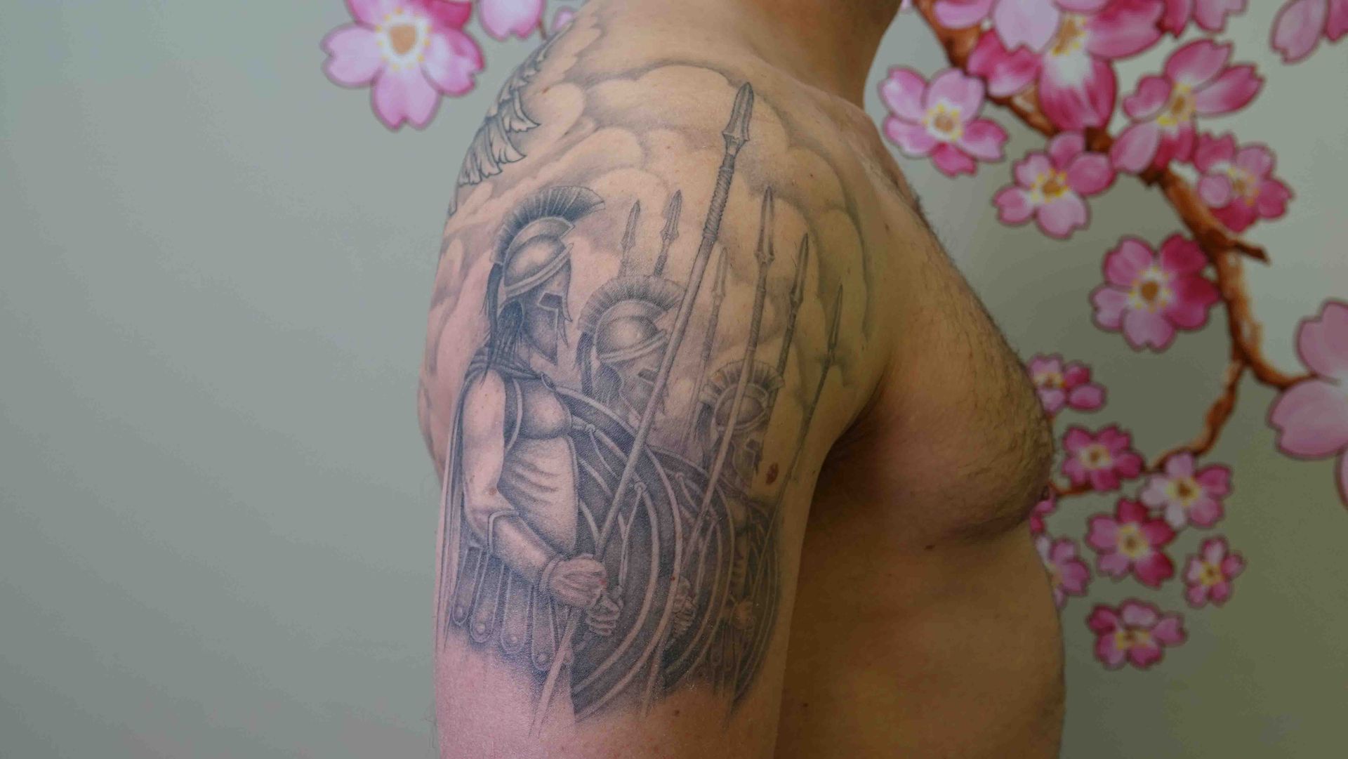 Zwart-grijze tatoeage op een schouder met een menselijke figuur tussen lange lijnen