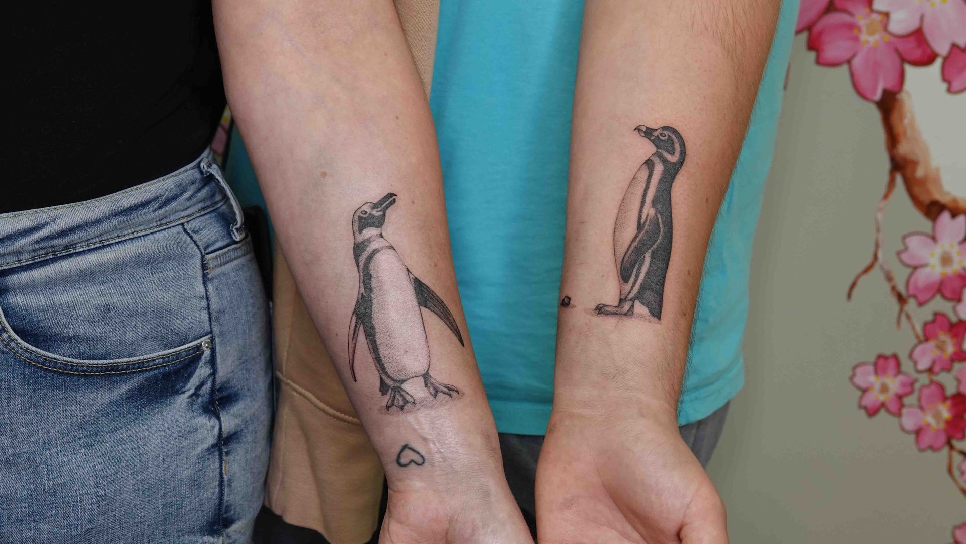 Twee onderarmen naast elkaar met dezelfde pinguïntatoeage