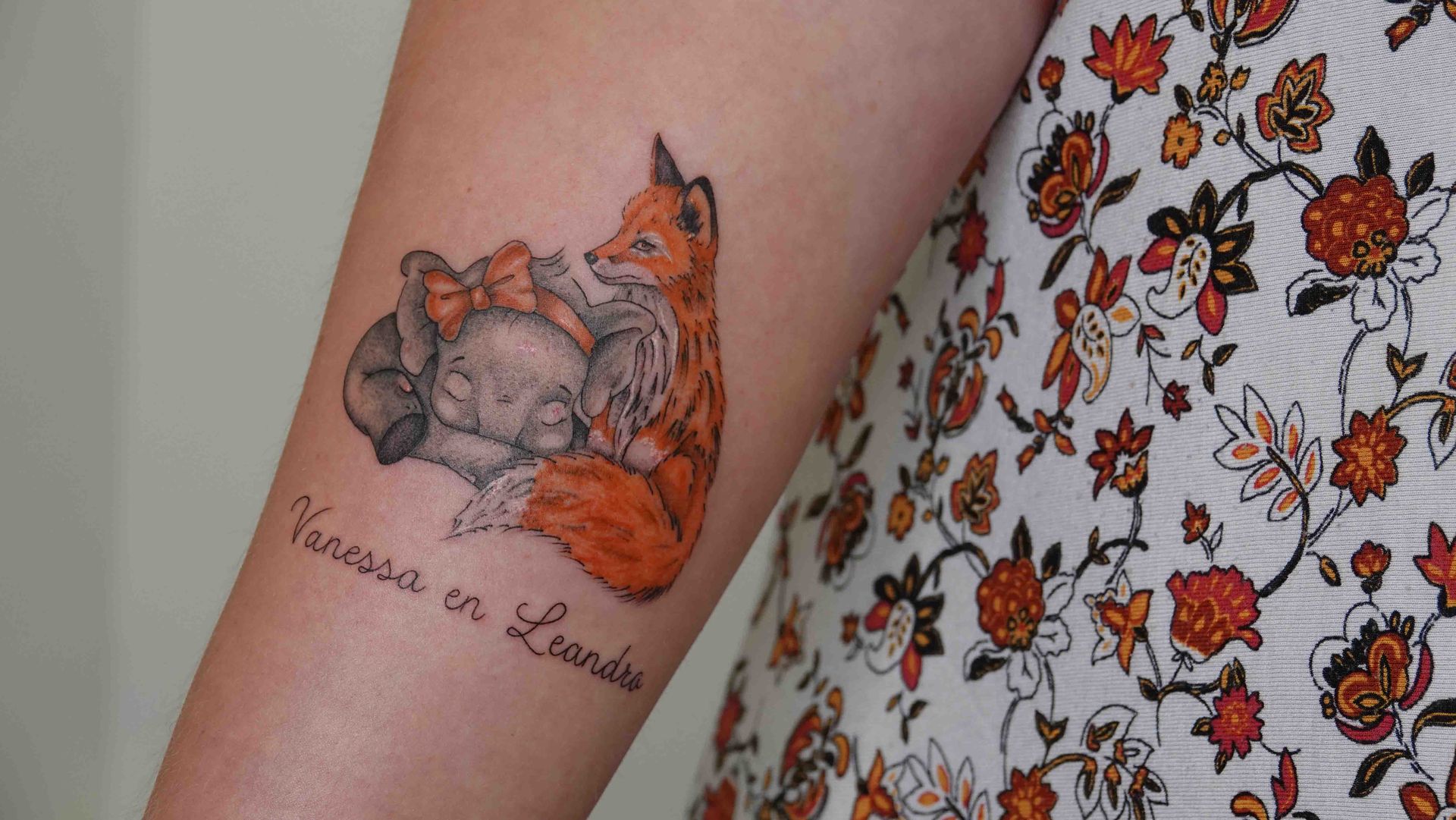 Slapend vosje in kleur op een bovenarm, met twee namen eronder
