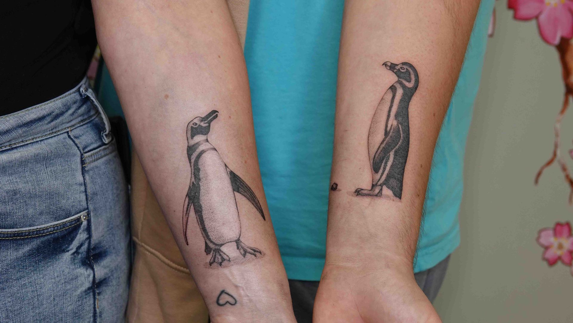 Twee onderarmen naast elkaar met dezelfde pinguïntatoeage