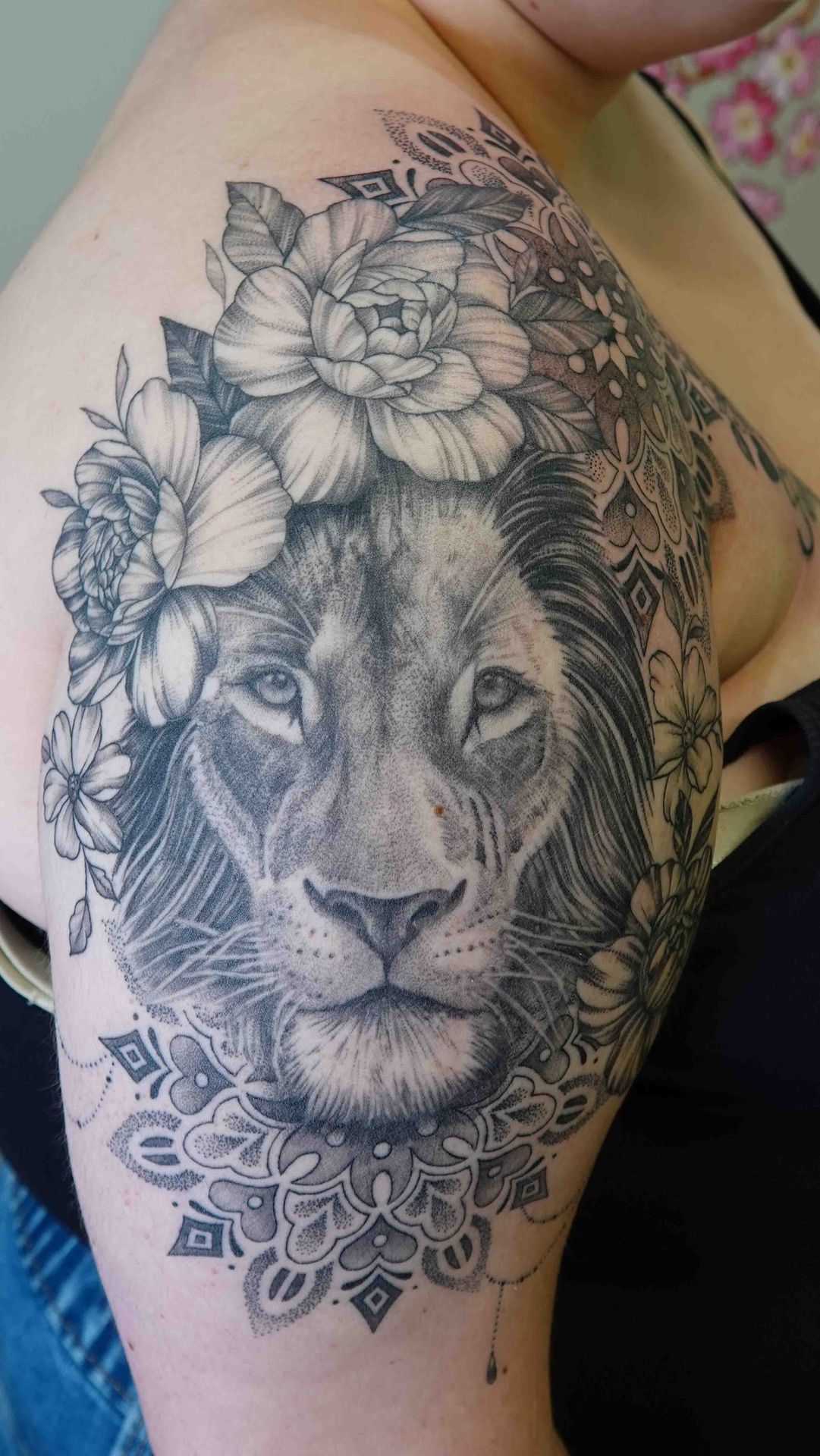 Leeuwenkop met een bloemenkrans en een mandala, op een bovenarm
