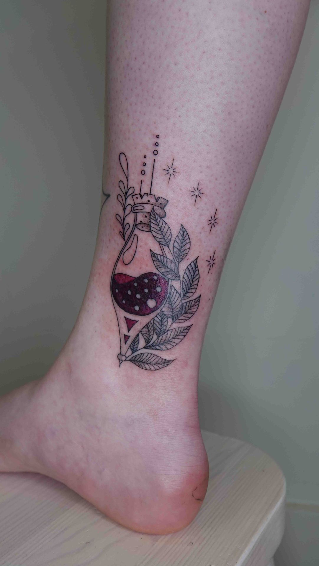 Cocktailglas met een rode drank, blaadjes en sterretjes, getatoeëerd op een enkel