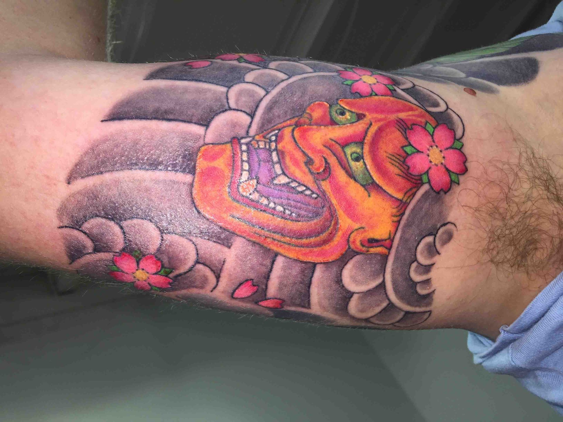 Oranjerood Japans hannya-masker met kersenbloesem en grijze wolken op de binnenkant van een arm