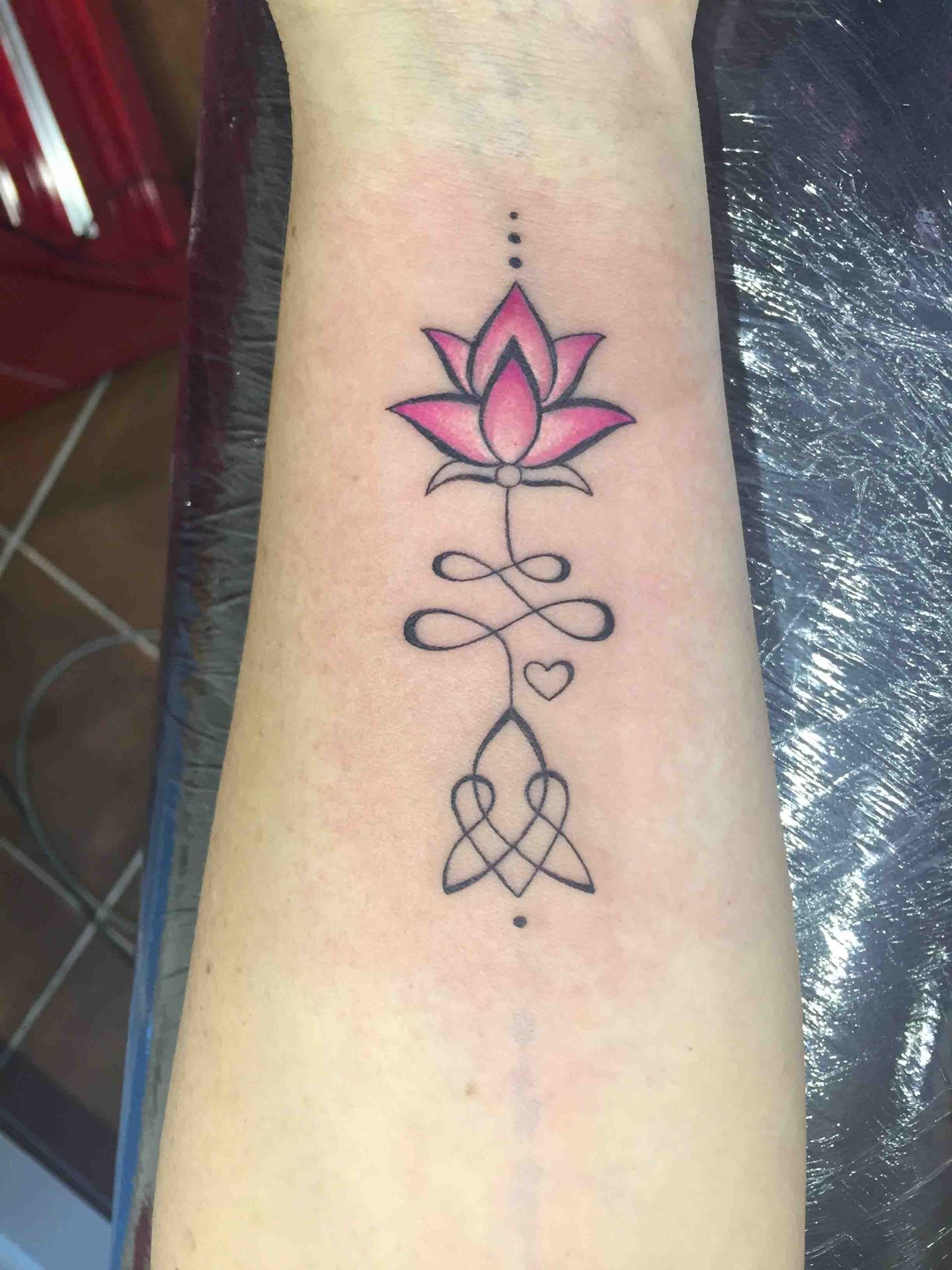 Roze lotusbloem boven een unalome-symbool en een knoop, op een onderarm