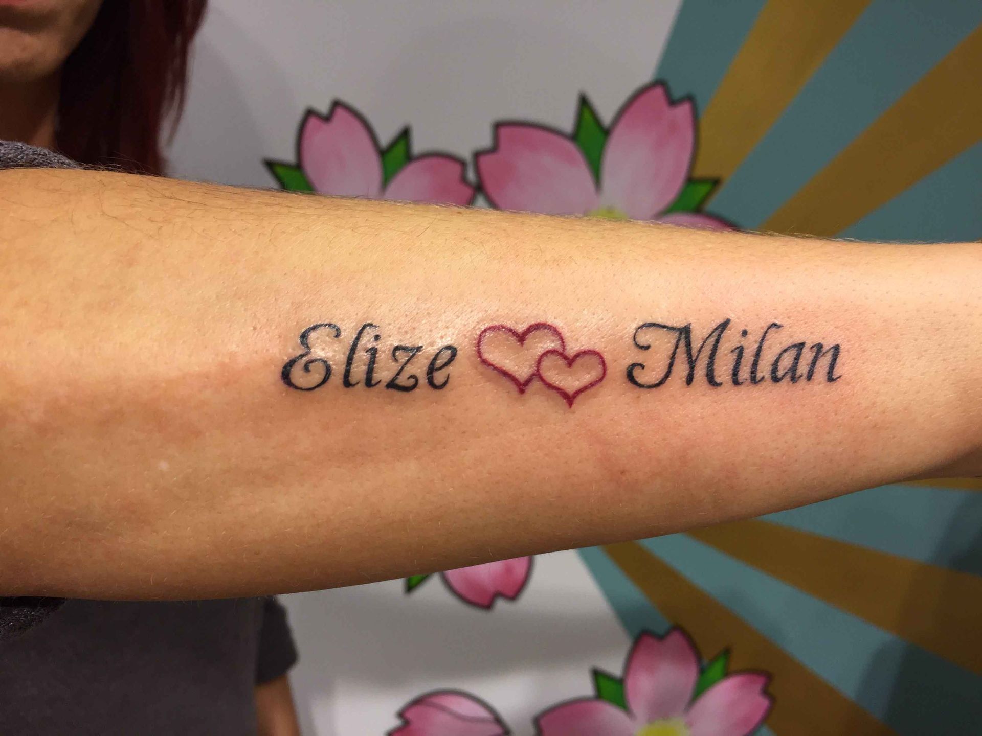 De namen Elize en Milan met twee hartjes ertussen, op een onderarm