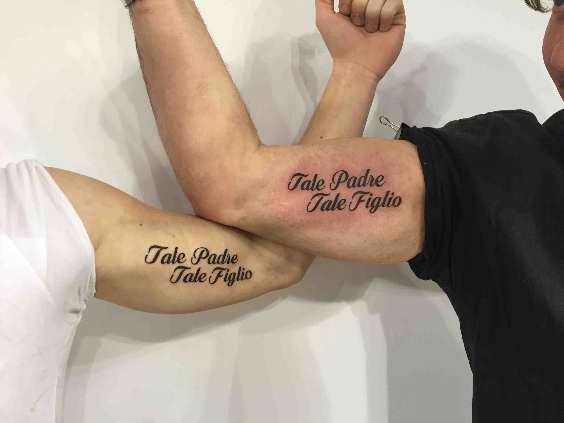 Twee armen naast elkaar met dezelfde tekst Tale padre tale figlio