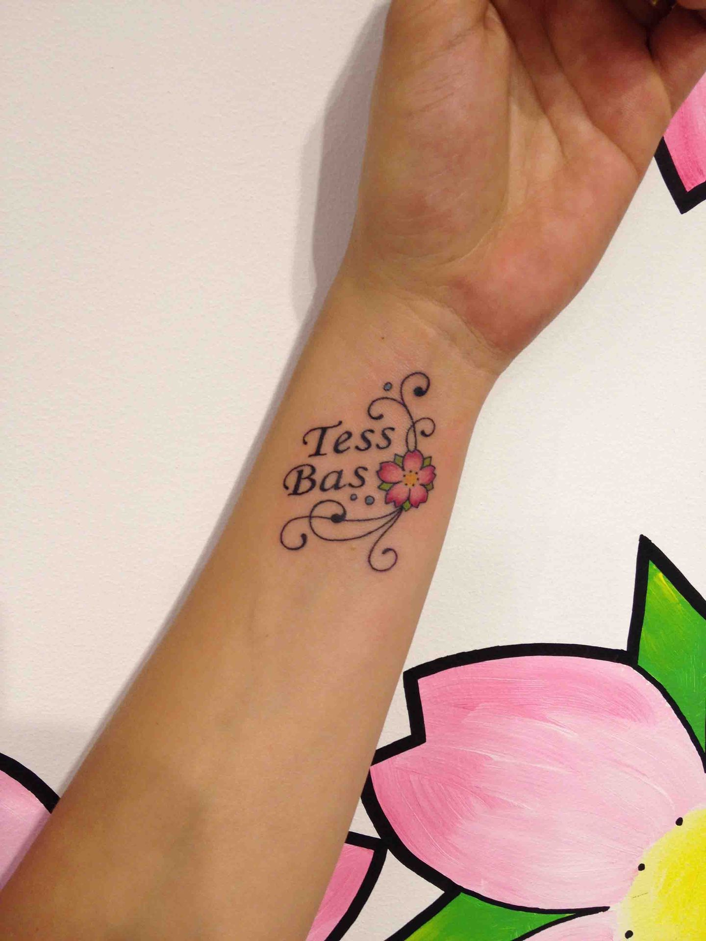 De namen Tess en Bas met een bloemenkrul op een pols