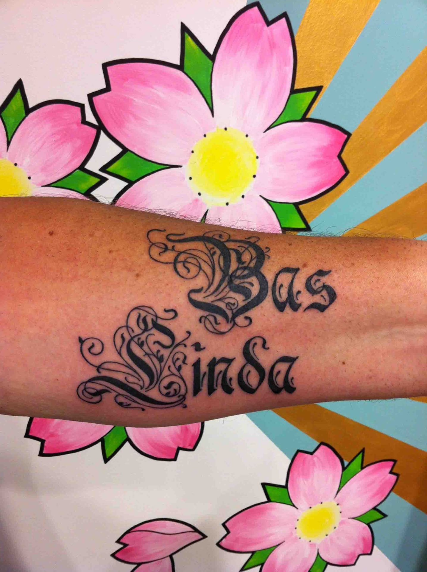 De namen Bas en Linda in sierlijke kalligrafie op een onderarm