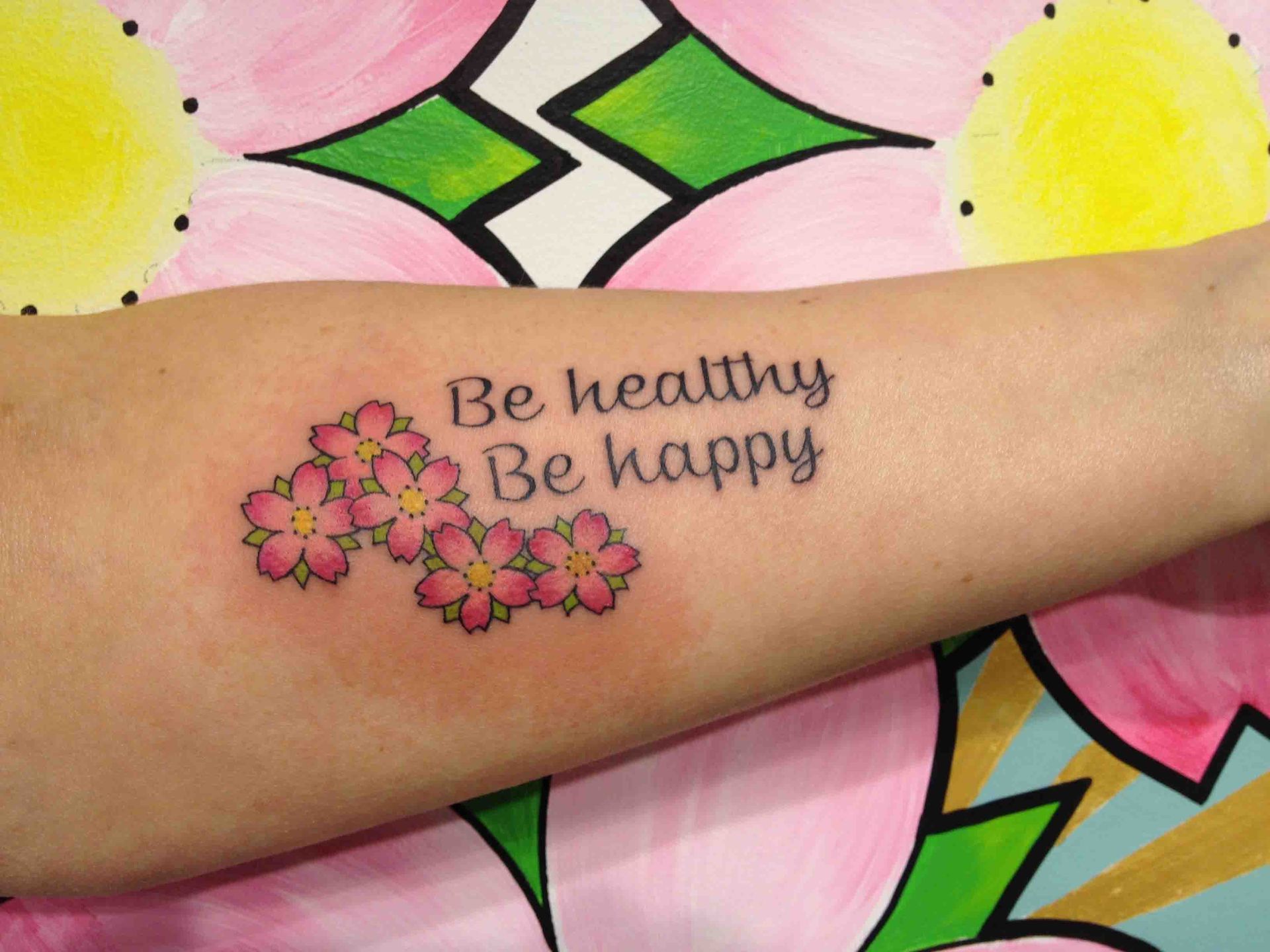 De woorden Be healthy be happy met kleine roze bloesems op een onderarm