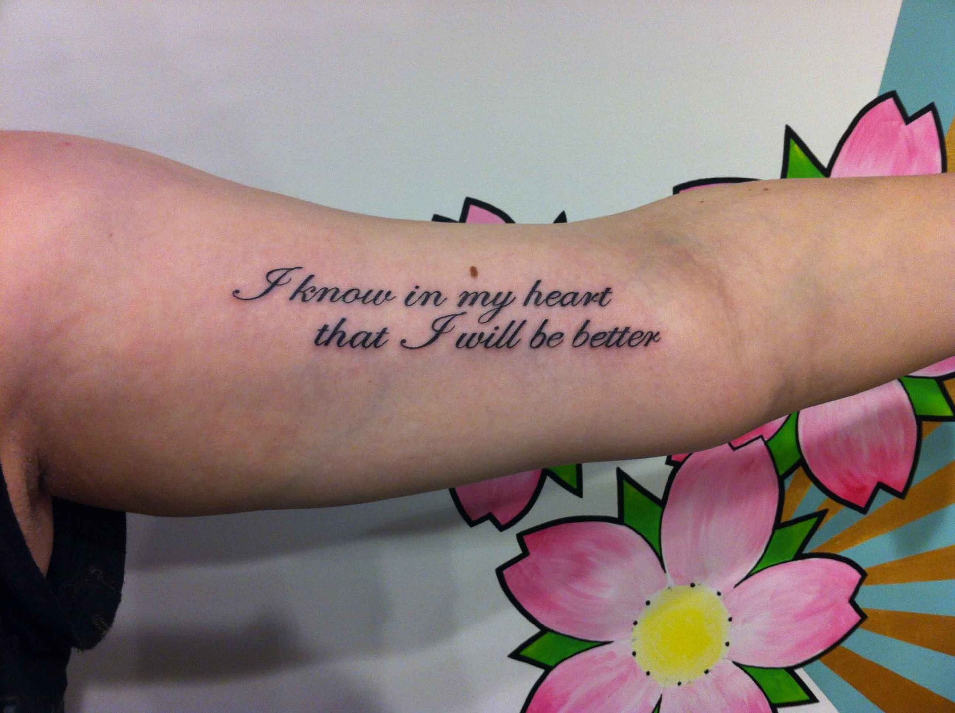 Tekst in schuinschrift op een onderarm: I know in my heart that I will be better