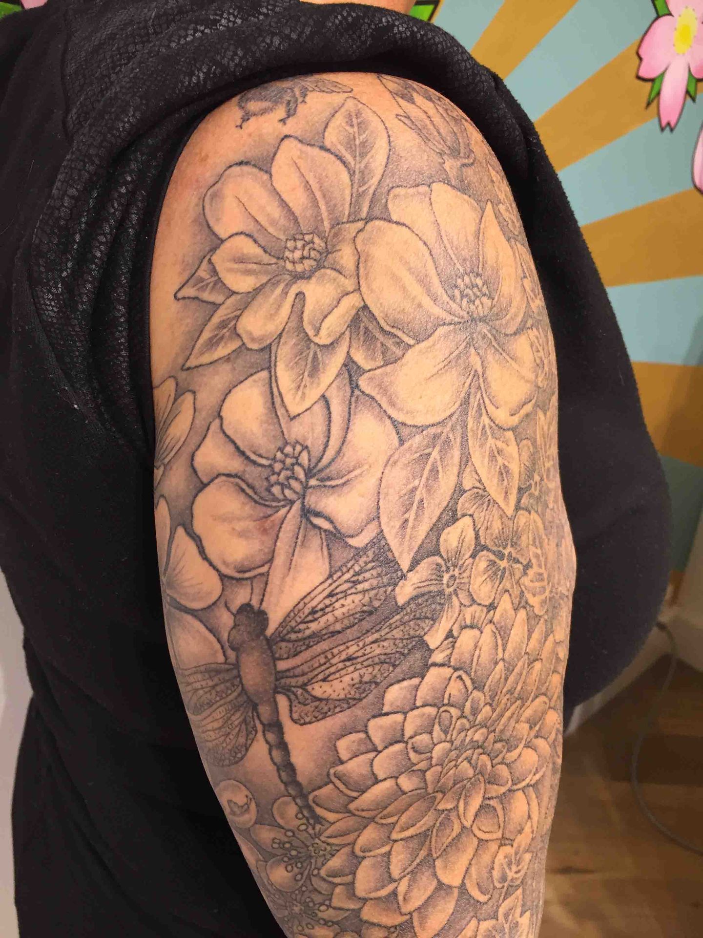 Schouder en bovenarm vol grote bloemen met een bij ertussen