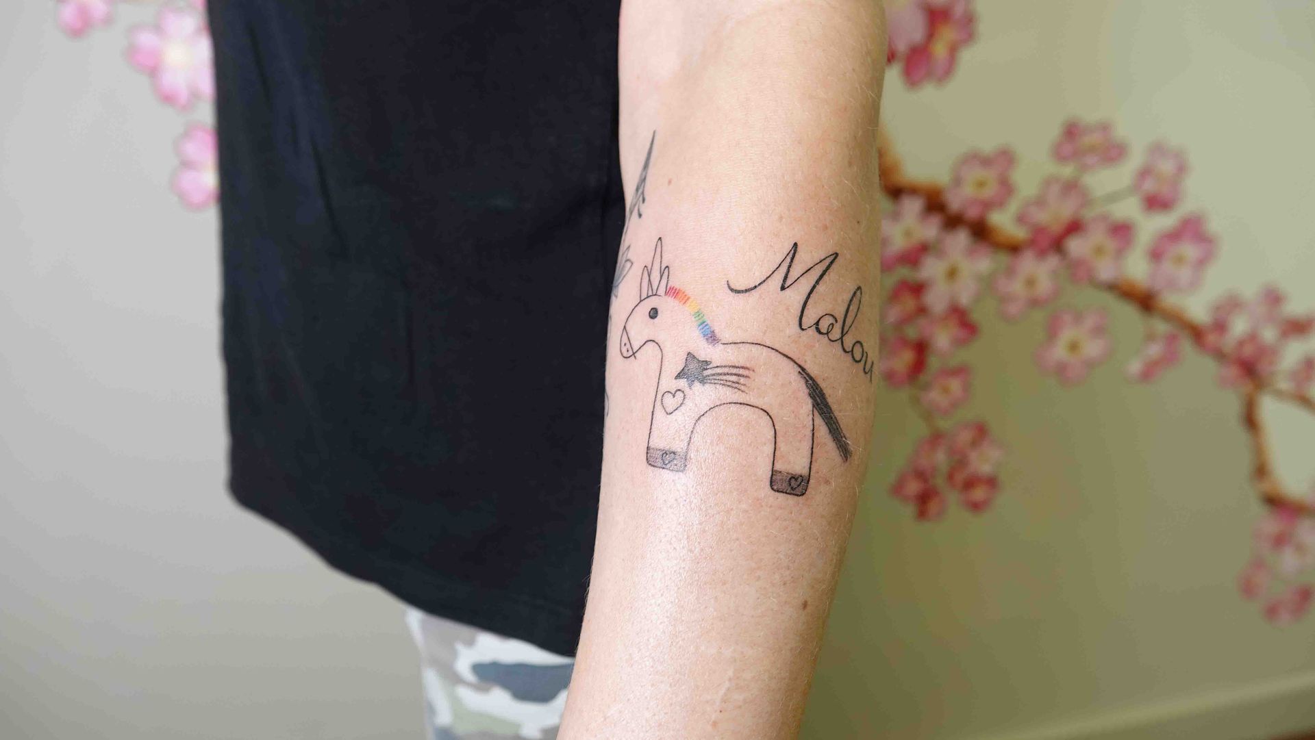 Lijntekening van een ezeltje met een naam erboven, op een onderarm