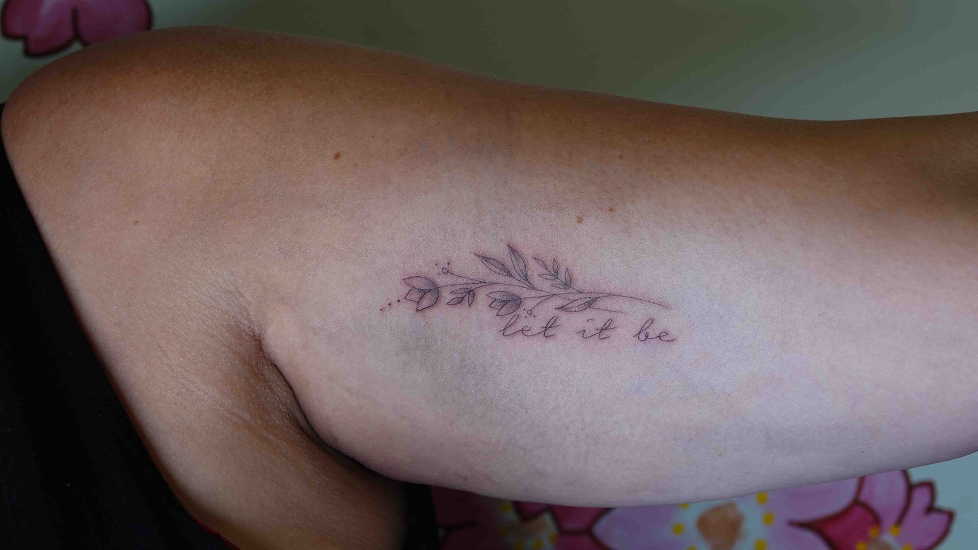 Bloementak met de woorden let it be op een bovenarm
